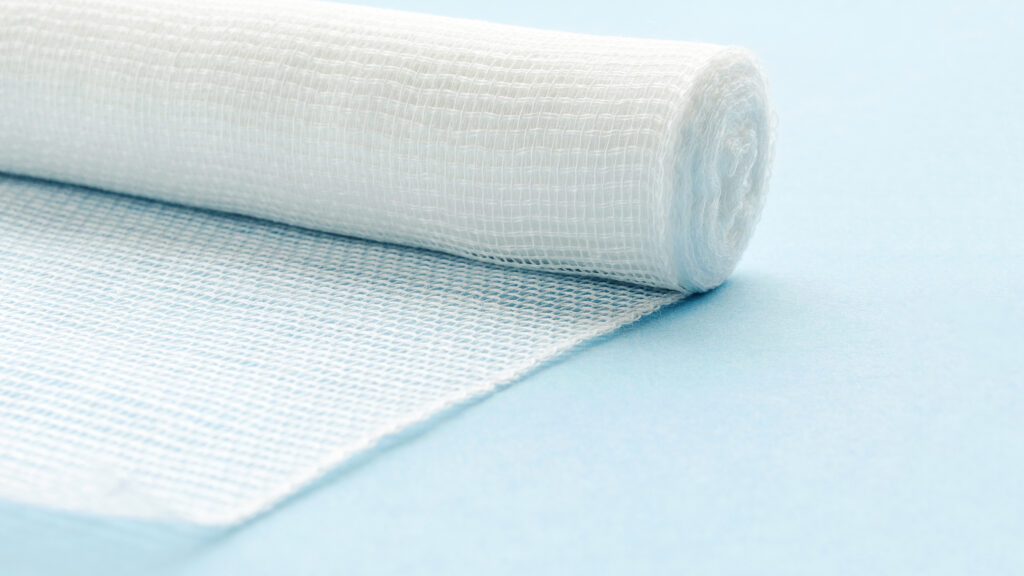 Sterile bandage on a blue background. White medical cotton bandage on a blue background. First aid - a white unfolded gauze bandage. White cotton bandage isolated on blue background